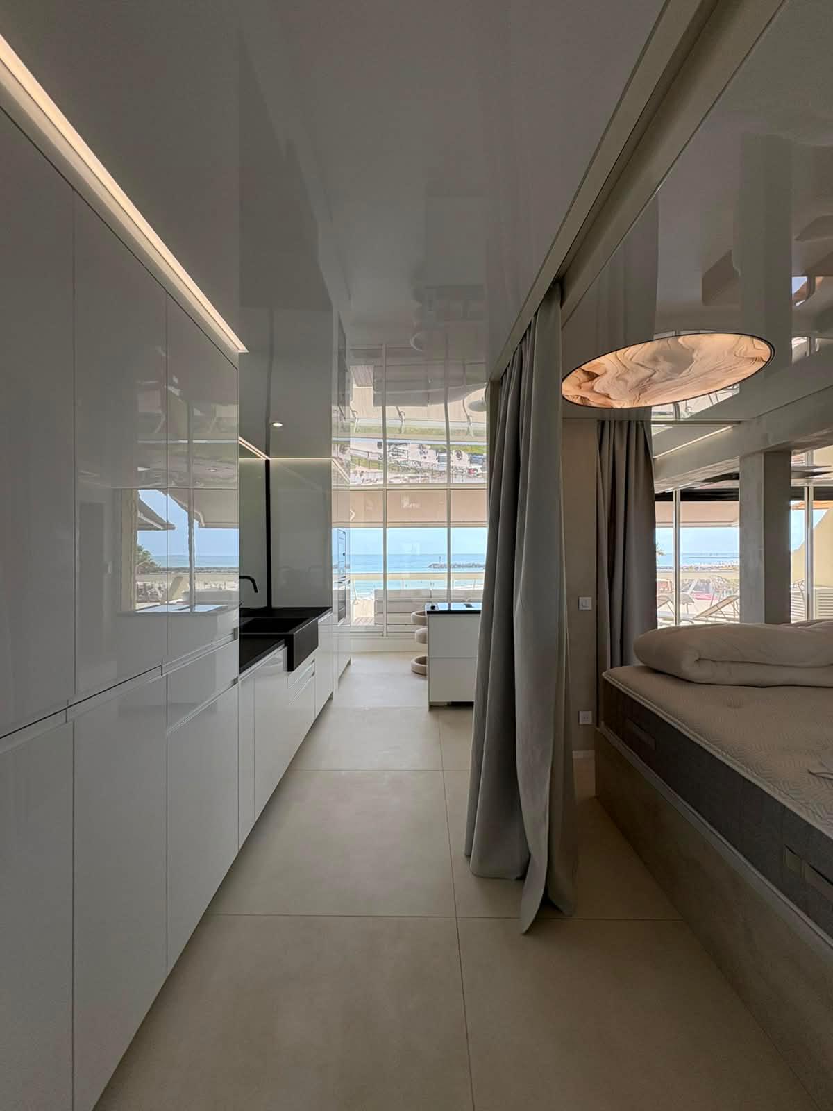 Enfilade intérieure : cuisine, coin nuit et baies vitrées ouvertes sur la mer