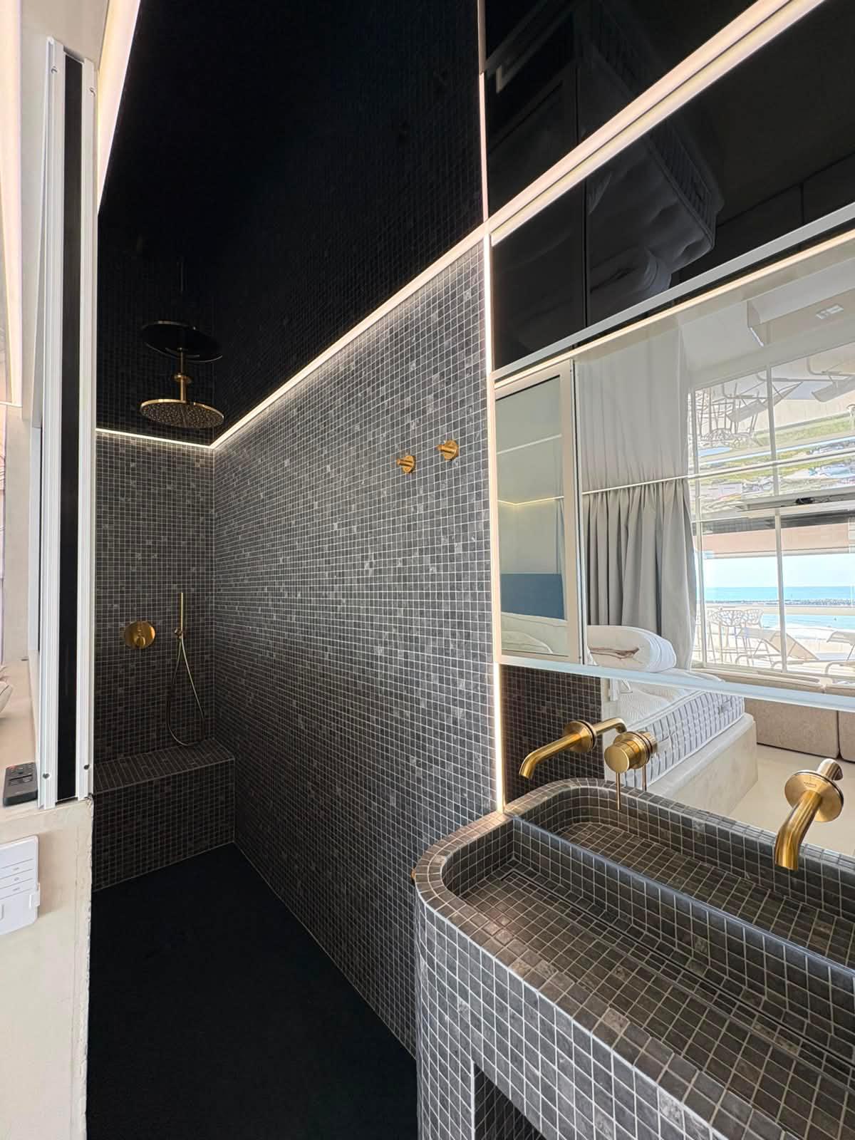 Salle d'eau en mosaïque sombre avec douche à l'italienne et robinetterie dorée